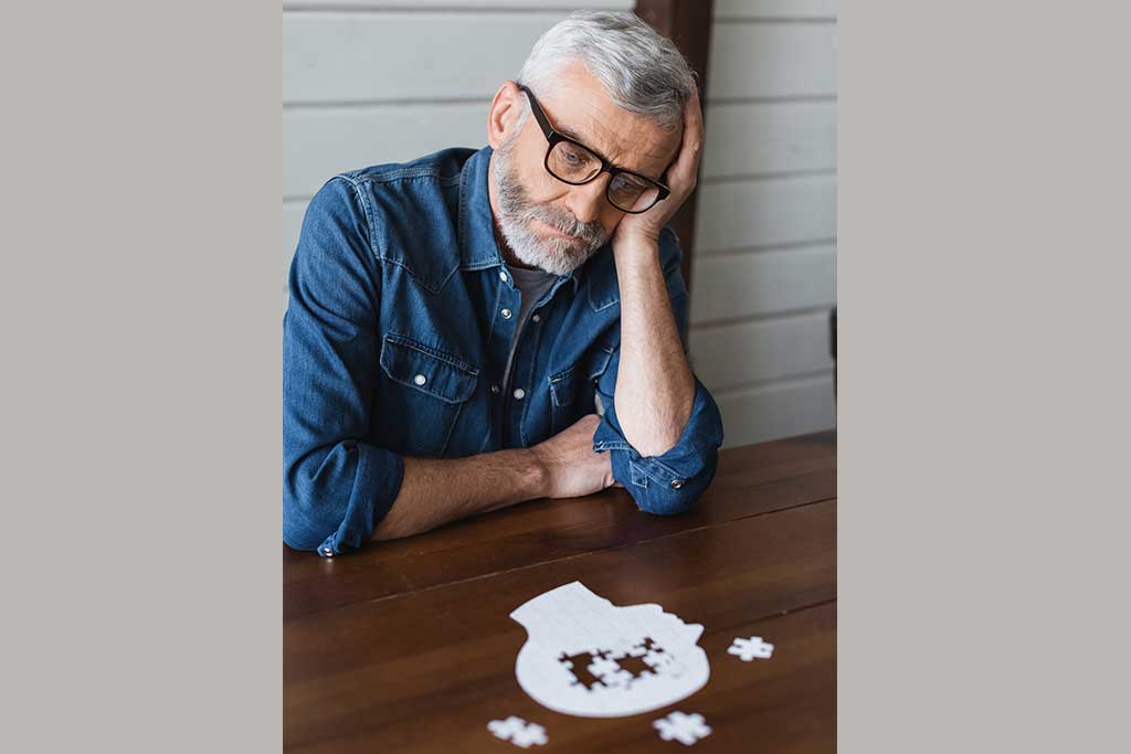Sad senior man with dementia looking at jigsaw on table